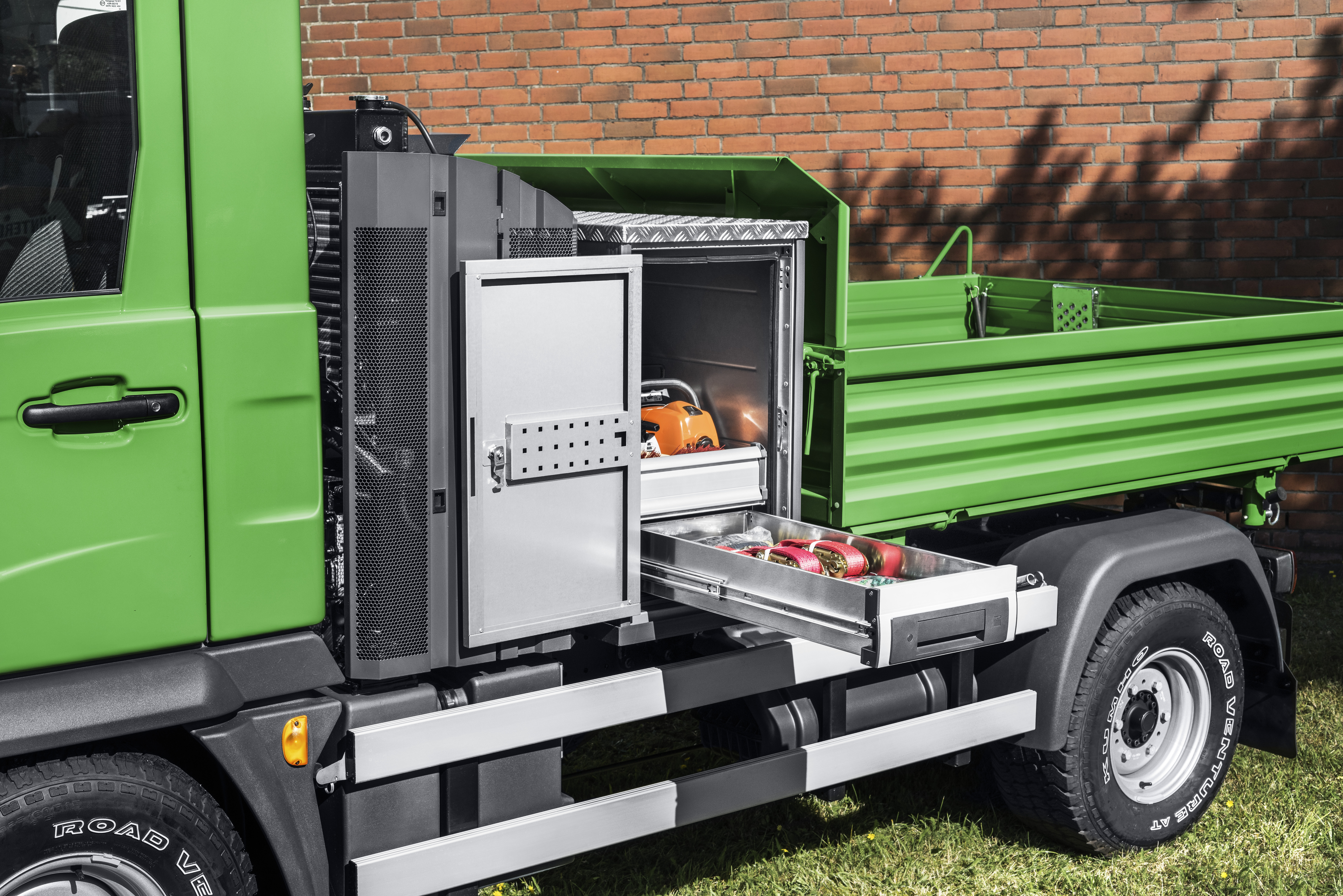 A green Multicar with a bottTainer in front of a fully loaded flatbed body, filled with tools and with a drawer pulled out.