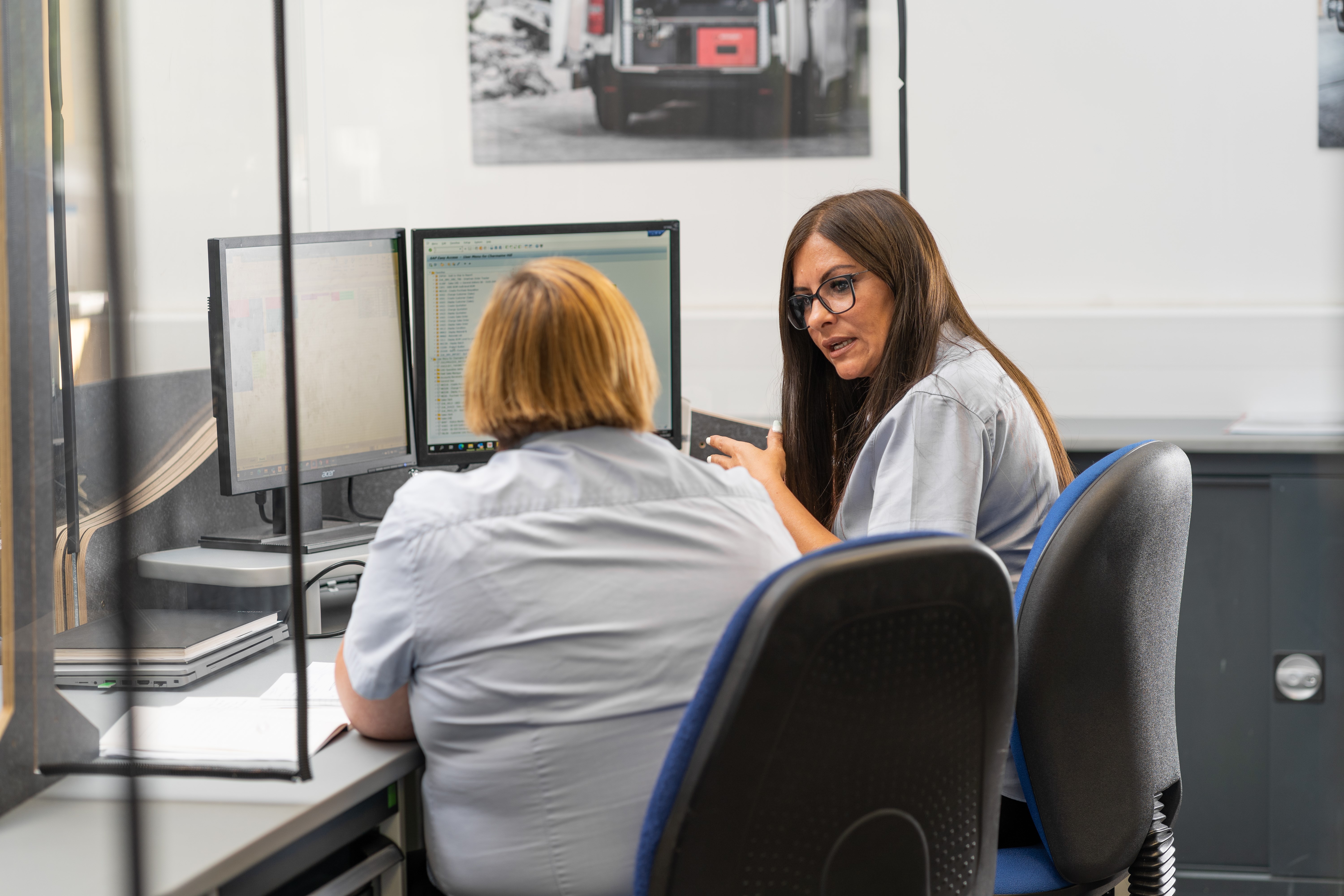 two bott employees at desk discussing van racking and workplace storage infront of two computer screens